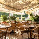 Terrasse de restaurant élégante en été, avec mobilier confortable, plantes en pots et une ambiance ombragée chaleureuse, lumière douce et reflets sur les tables.