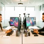 Une femme et un homme collaborent dans un bureau moderne et lumineux, entourés d’écrans, de casques et d’accessoires informatiques.